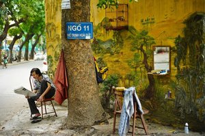 A Vietnamese Street Barber Reads A Newspaper While Waiting For Customers In Hanoi — Morgan Ommer